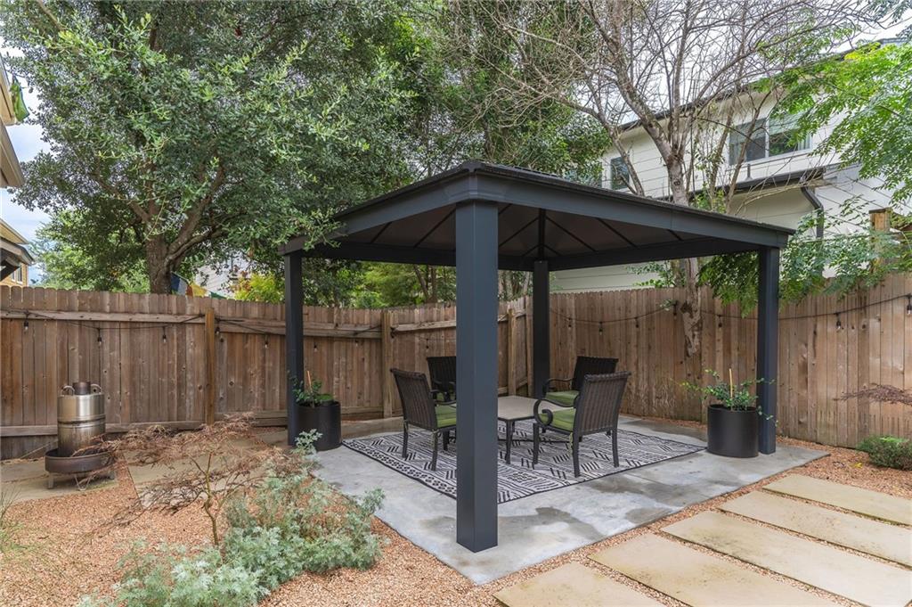 6708 Menchaca Road, Unit 14 Austin, TX 78745 - Photo 2 of 22 Private backyard featuring a dark-toned gazebo with concrete flooring, surrounded by a wood fence, pea gravel, and mature trees