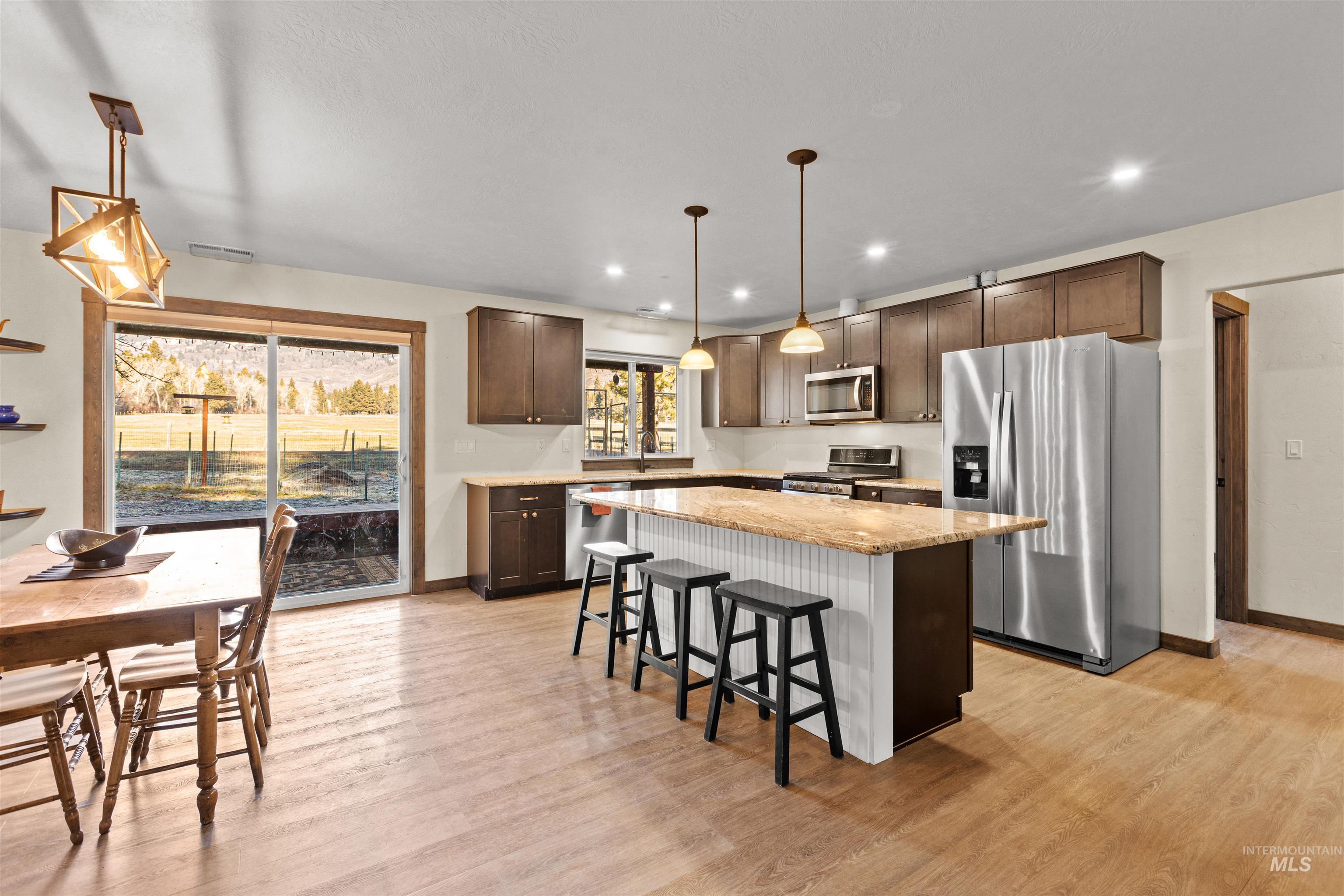 3488 Ward Road Cambridge, ID 83610 - Photo 16 of 49 Kitchen featuring appliances with stainless steel finishes, a breakfast bar, dark brown cabinetry, a center island, and light stone counters