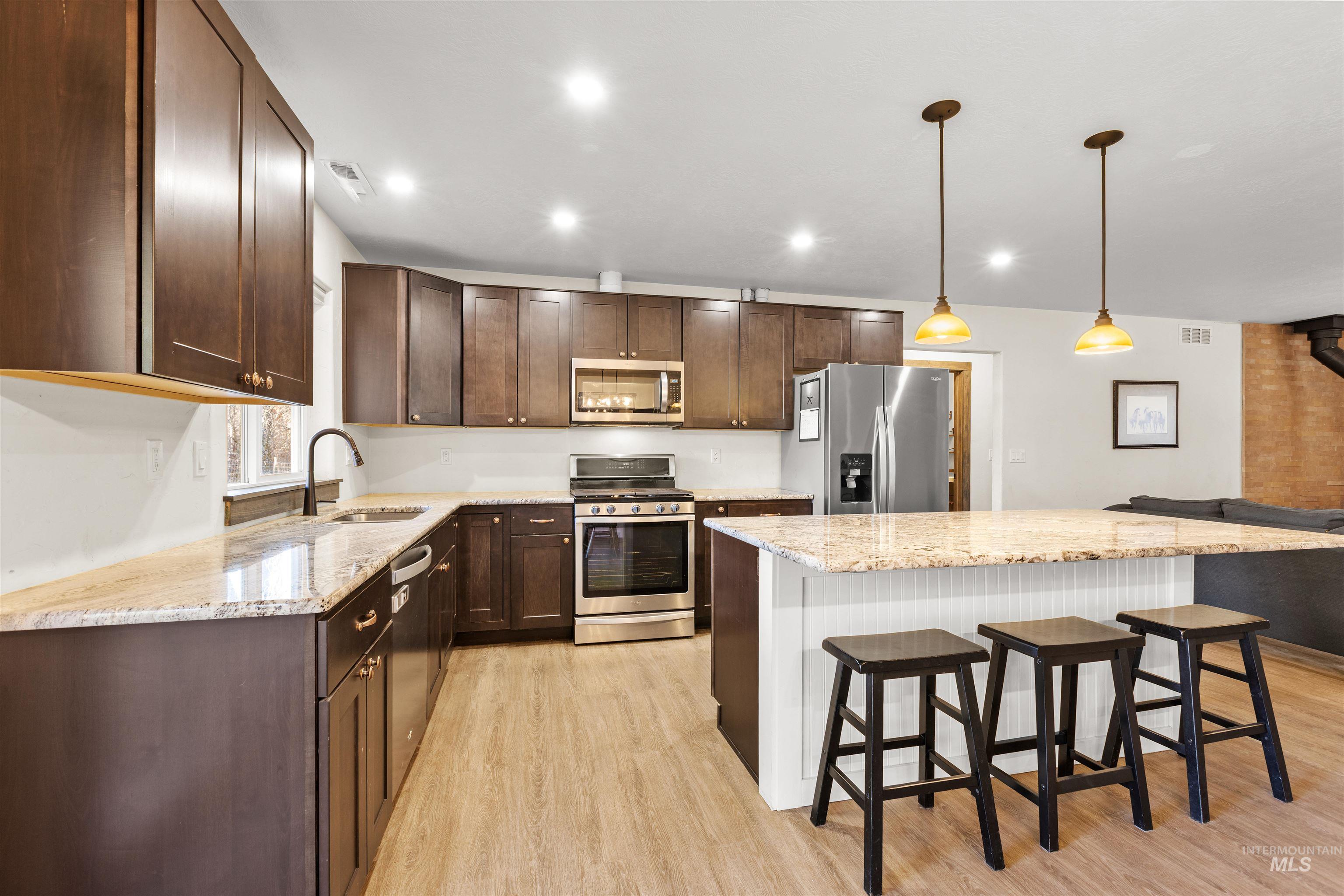 3488 Ward Road Cambridge, ID 83610 - Photo 17 of 49 Kitchen featuring appliances with stainless steel finishes, light stone countertops, dark brown cabinets, a kitchen breakfast bar, and recessed lighting