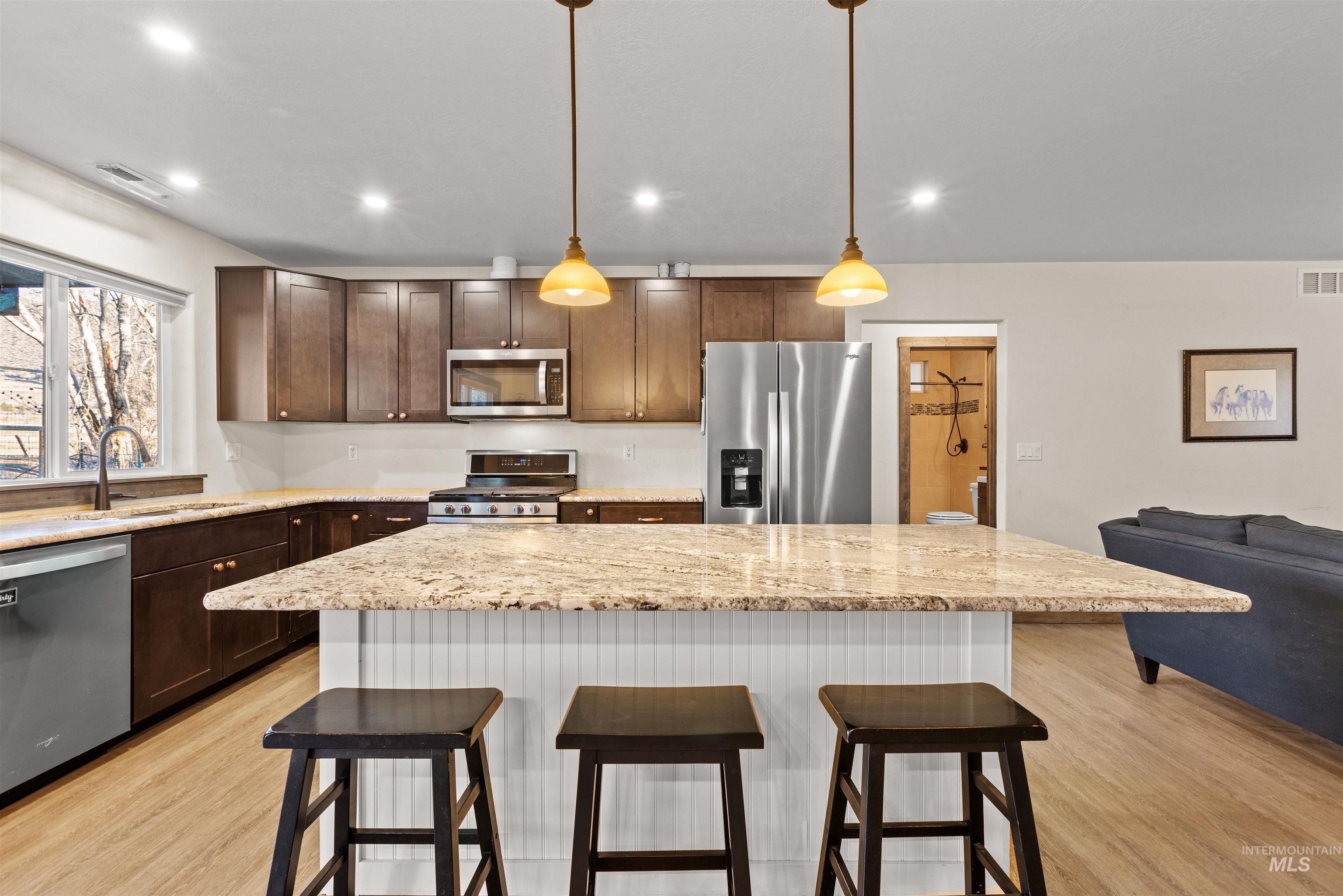 3488 Ward Road Cambridge, ID 83610 - Photo 20 of 49 Kitchen featuring a kitchen bar, a center island, light stone countertops, stainless steel appliances, and hanging light fixtures