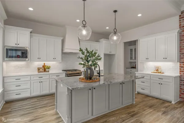 a kitchen with kitchen island granite countertop a stove a sink and white cabinets with wooden floor