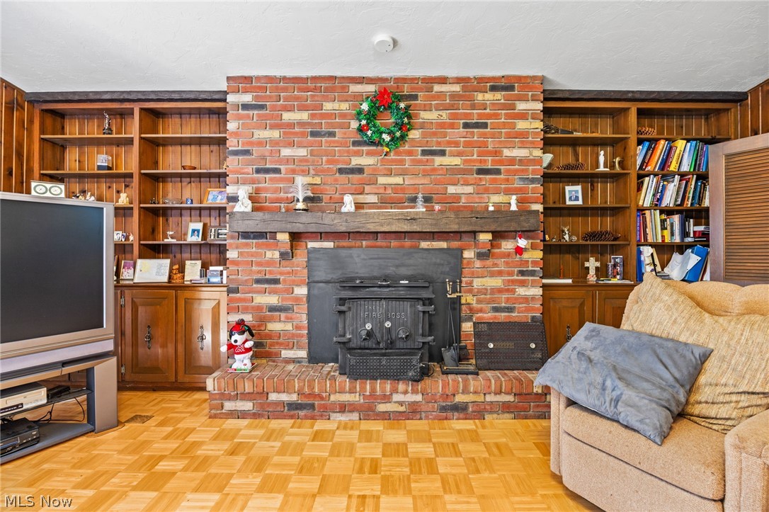 3070 Hamilton Road Medina, OH 44256 - Photo 19 of 34 Brick fireplace with wood-burning stove, flanked by built-in wood shelving and cabinetry, all set upon wood-finish parquet flooring