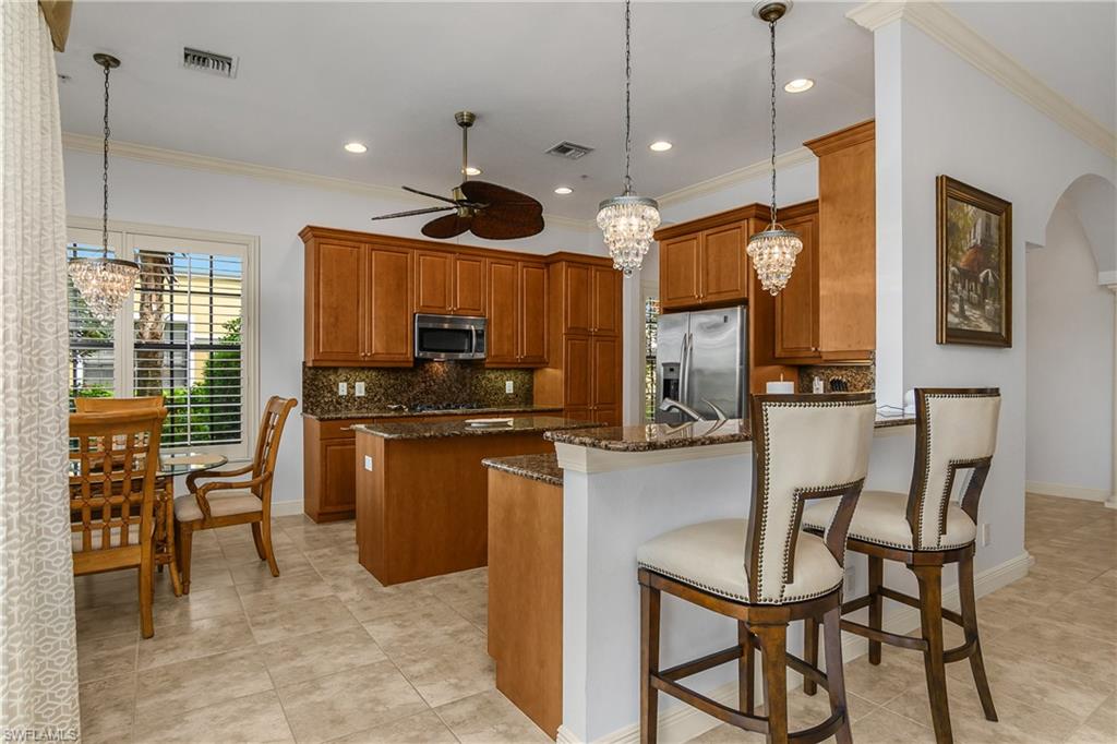 9109 Prima Way, Unit 102 Naples, FL 34113 - Photo 8 of 50 a kitchen with stainless steel appliances kitchen island granite countertop a table chairs and a refrigerator