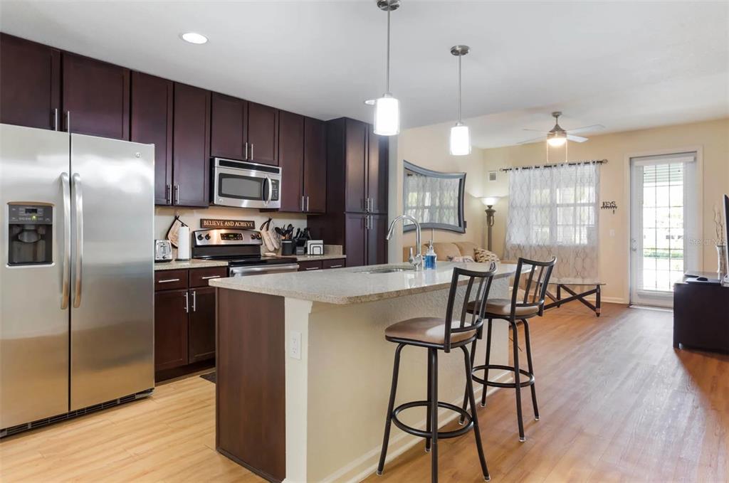 3334 South Bismark Lane, Unit 1B01304 Jupiter, FL 33458 - Photo 20 of 36 a kitchen with stainless steel appliances kitchen island granite countertop a refrigerator a stove a sink a dining table and chairs with wooden floor