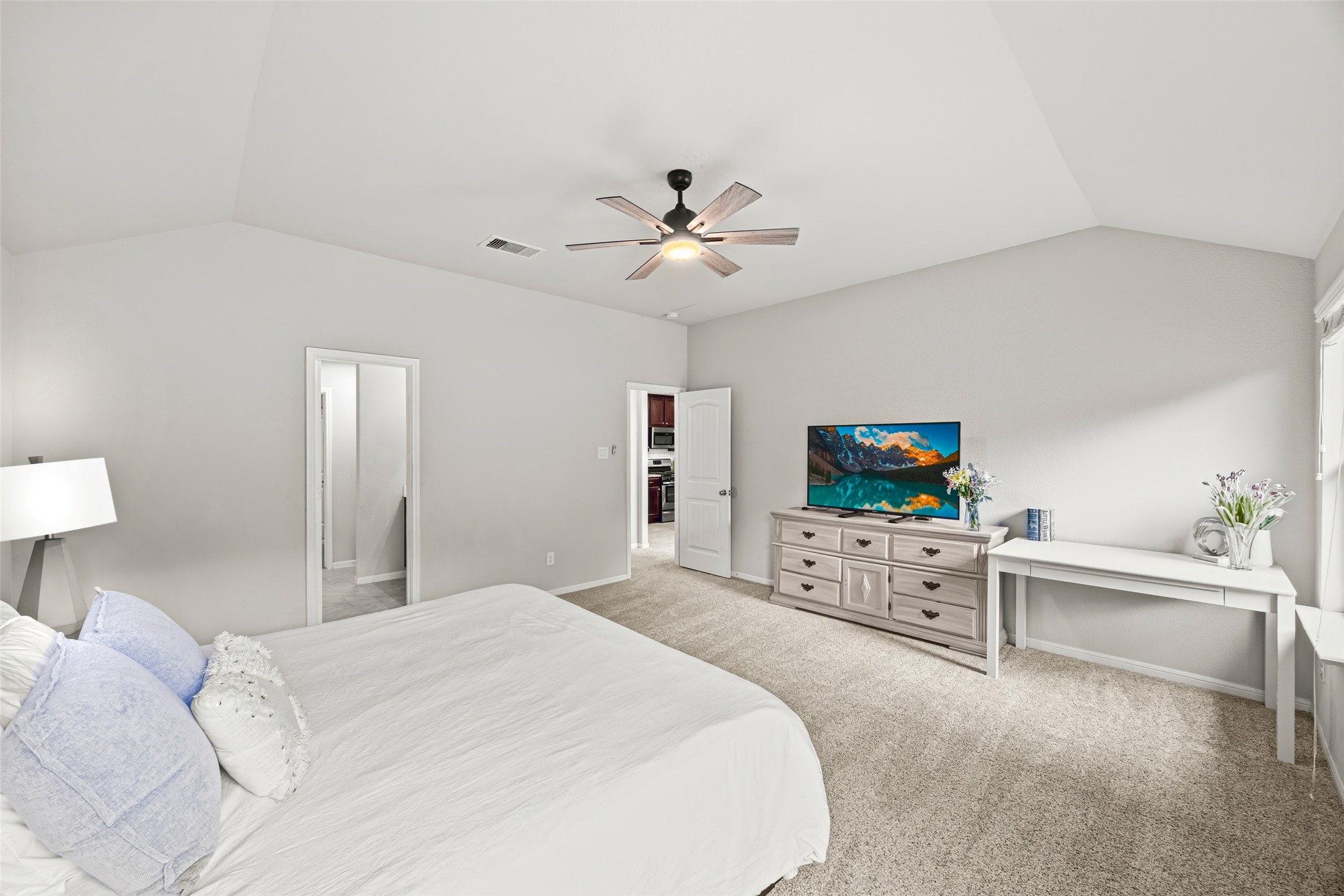 8026 Farthing Lane Rosharon, TX 77583 - Photo 7 of 13 This spacious bedroom features neutral tones, a ceiling fan, and ample natural light. It includes a cozy carpeted floor, a stylish dresser with a TV, and a small desk area perfect for work or decor.