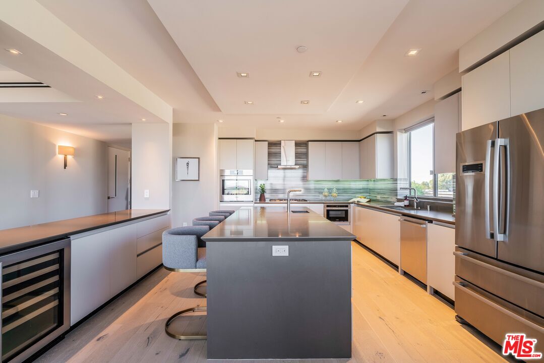 a kitchen with stainless steel appliances granite countertop a refrigerator a sink dishwasher a stove and white countertops with wooden floor