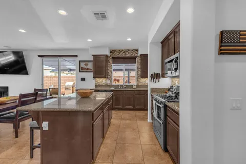 a kitchen with stainless steel appliances granite countertop a stove top oven a sink dishwasher a dining table and chairs with wooden floor