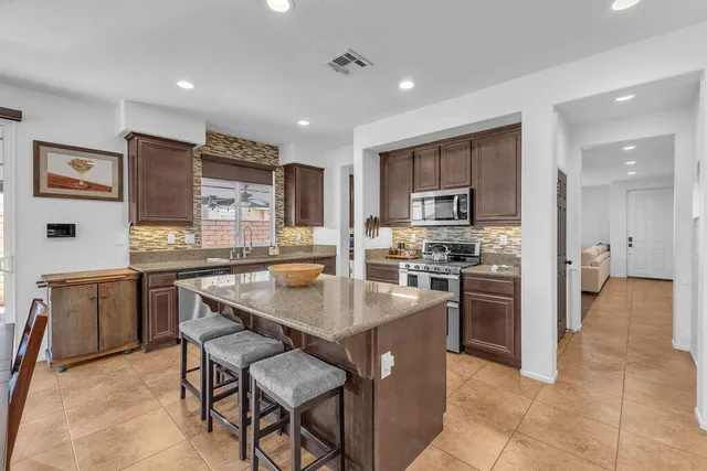 a kitchen with stainless steel appliances granite countertop a refrigerator a stove and a sink with wooden cabinets