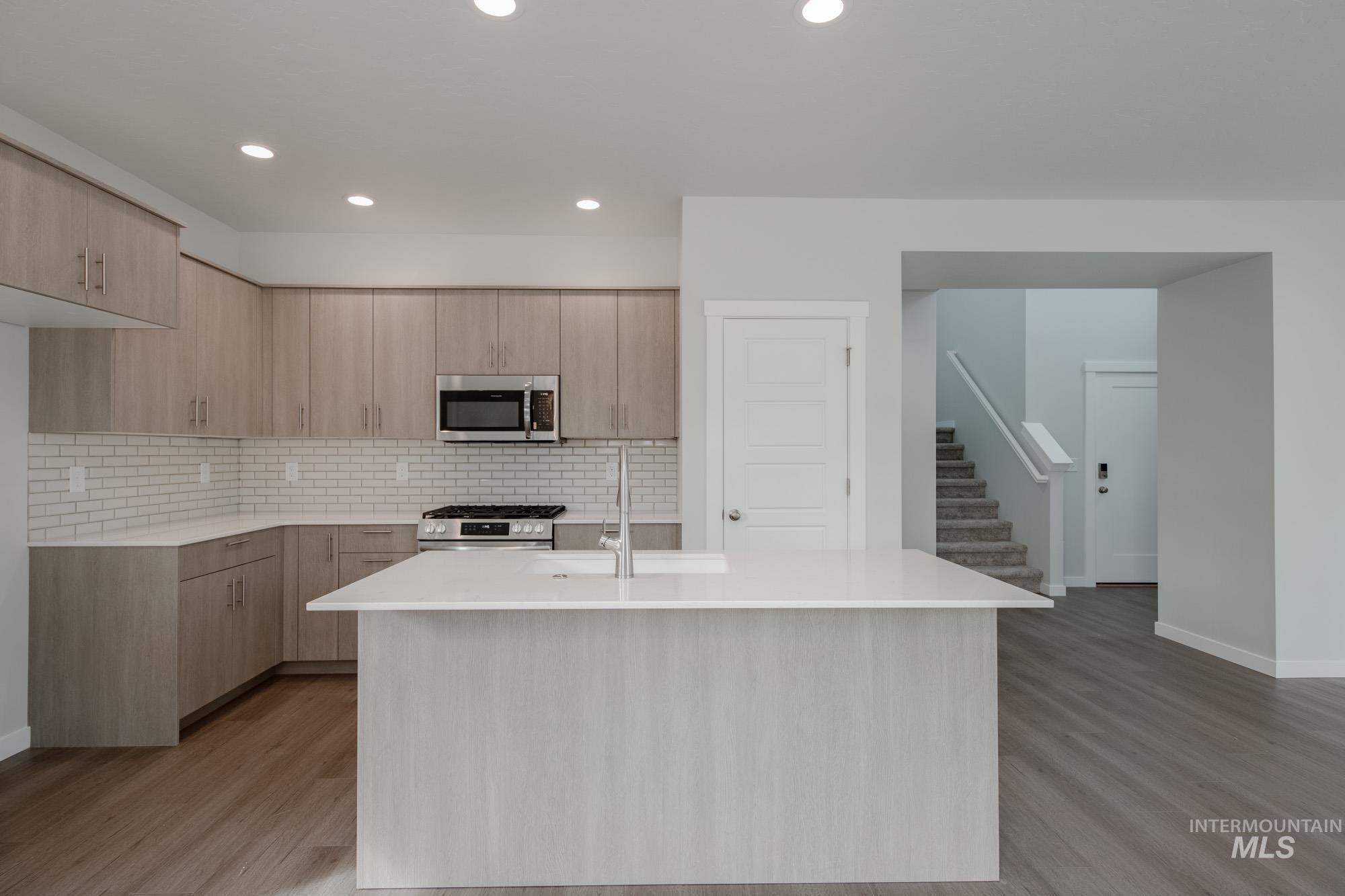 910 North Mirror Creek Way Meridian, ID 83642 - Photo 10 of 27 Kitchen featuring light brown cabinets, modern cabinets, light stone counters, a center island with sink, and backsplash