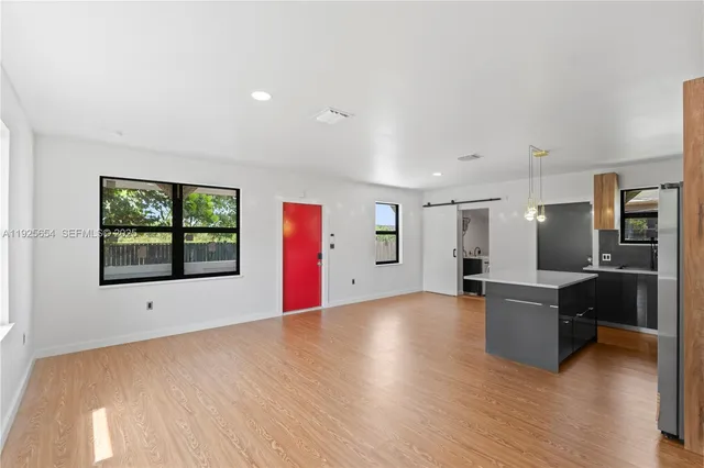 a view of an empty room with kitchen and window