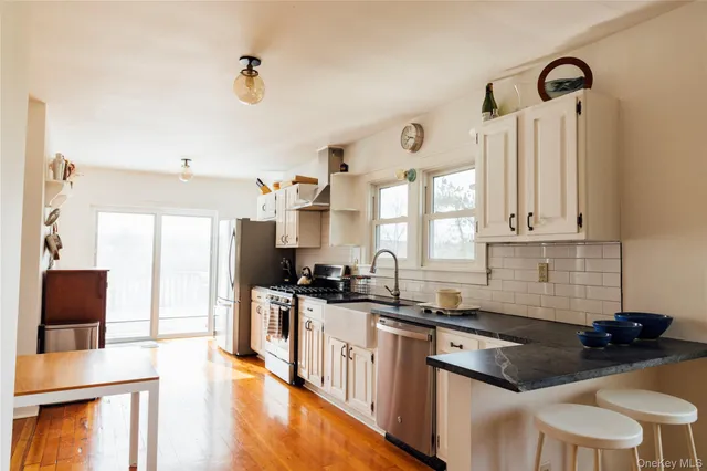 a kitchen with stainless steel appliances a stove a sink a stove a refrigerator cabinets and a dining table with wooden floor