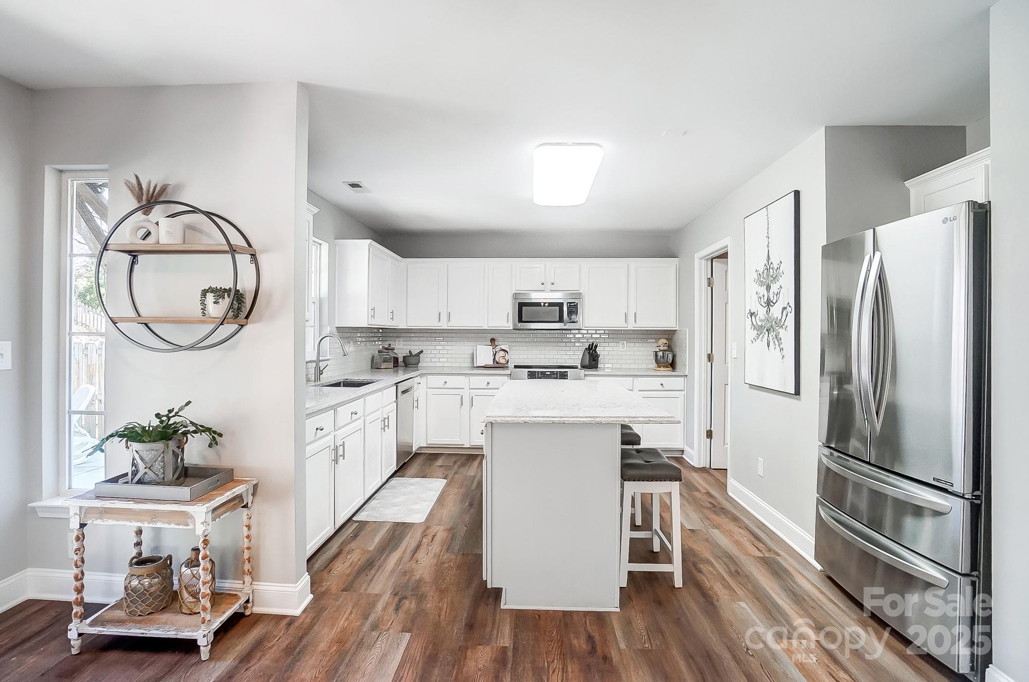 7647 Black Hawk Lane Tega Cay, SC 29708 - Photo 11 of 42 a kitchen with stainless steel appliances a refrigerator a stove a sink dishwasher and white cabinets with wooden floor
