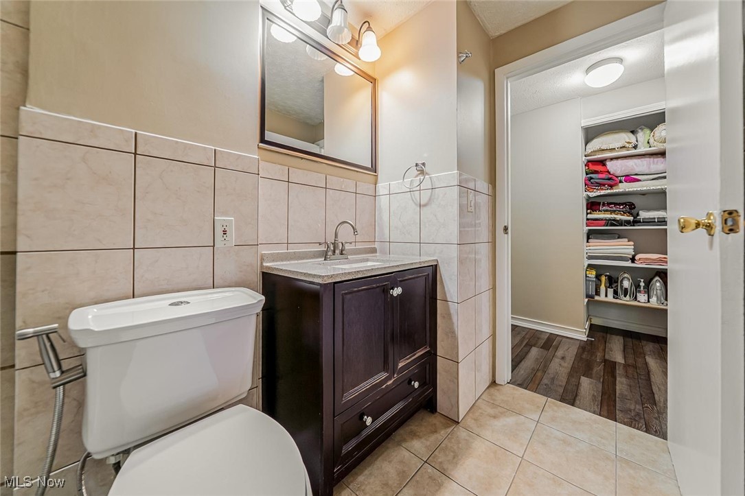 1489 Sunnyacres Road Akron, OH 44321 - Photo 17 of 33 Full bathroom featuring vanity, a spacious closet, tile walls, light tile patterned flooring, and a textured ceiling