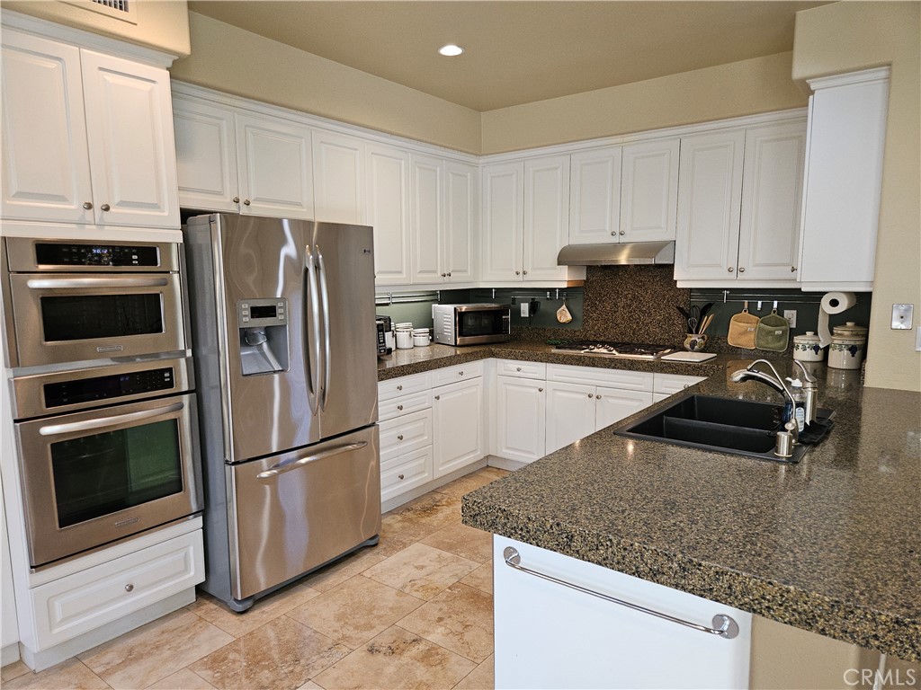 12924 Maxwell Drive Tustin, CA 92782 - Photo 3 of 8 a kitchen with granite countertop a refrigerator a stove a sink a counter space and cabinets