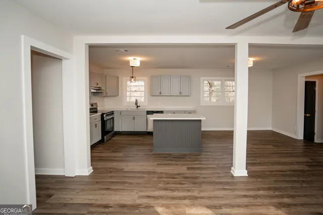 a view of a livingroom with a hardwood floor a ceiling fan and windows