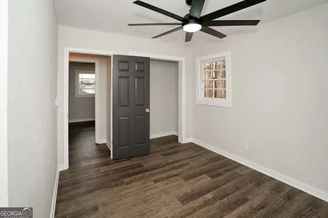 an empty room to hallway with wooden floor fan and a window
