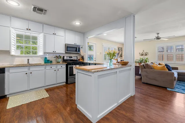 a kitchen with stainless steel appliances kitchen island granite countertop a stove a sink dishwasher a refrigerator and white cabinets with wooden floor