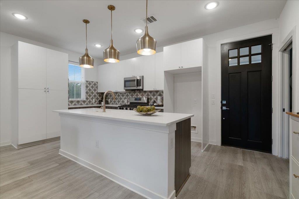 2624 Metcalfe Road, Unit 10 Austin, TX 78741 - Photo 5 of 27 Kitchen featuring white cabinetry, decorative light fixtures, stainless steel appliances, a kitchen island with sink, and light wood-type flooring