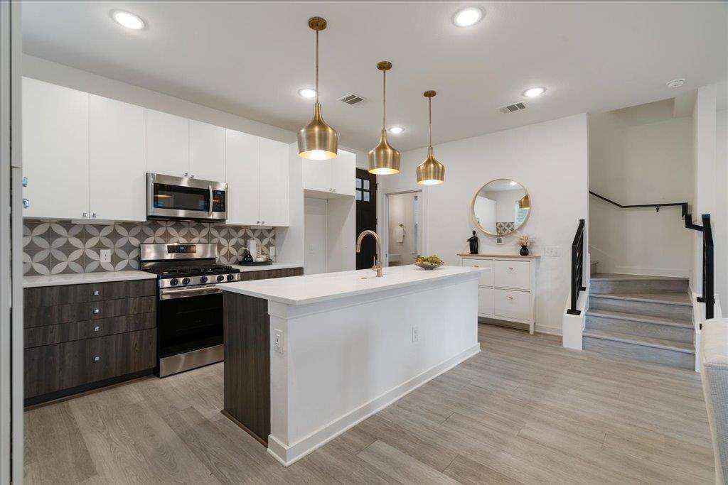 2624 Metcalfe Road, Unit 10 Austin, TX 78741 - Photo 6 of 27 Kitchen with appliances with stainless steel finishes, an island with sink, white cabinetry, pendant lighting, and decorative backsplash