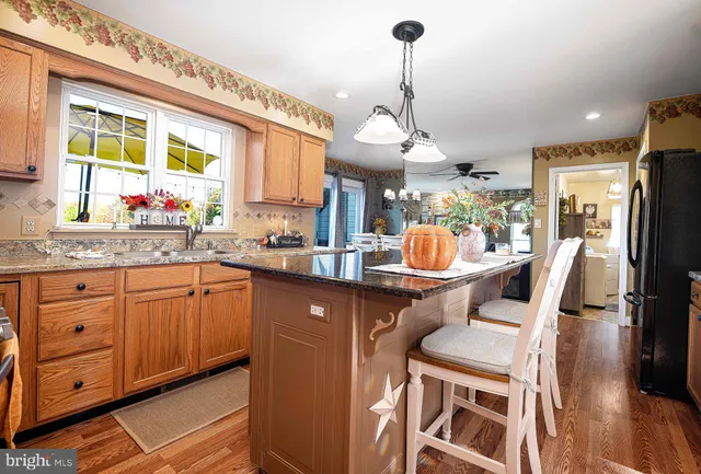 a kitchen with stainless steel appliances granite countertop a refrigerator a sink dishwasher a stove and a dining table with wooden floor