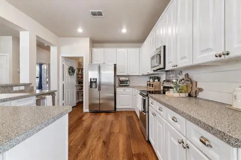 a kitchen with stainless steel appliances granite countertop a refrigerator a sink dishwasher and white cabinets with wooden floor