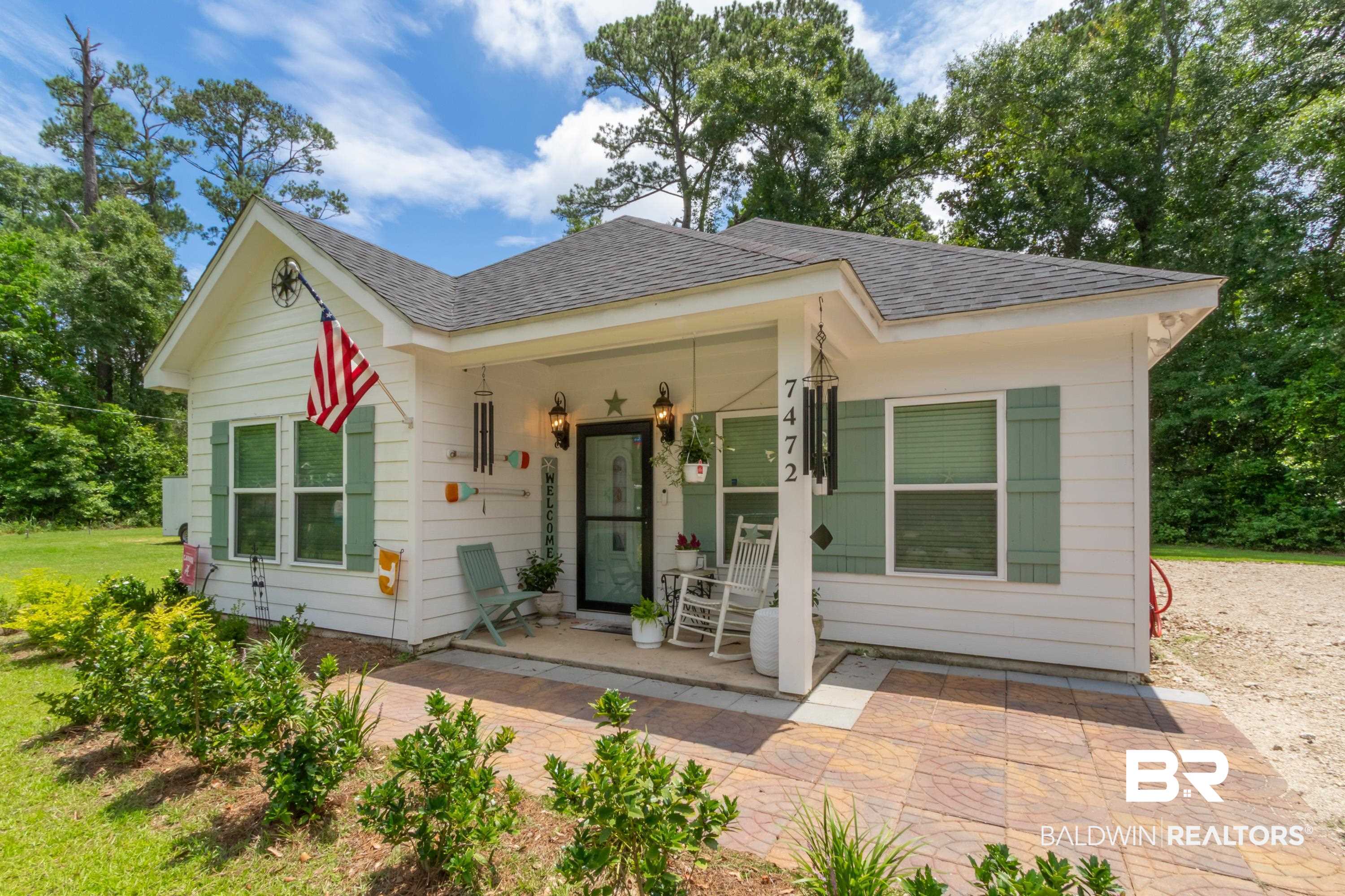 7472 Coopers Landing Road Foley, AL 36535 - Photo 40 of 40 White siding exterior with a covered front porch, dark gray roof shingles, light green window shutters, and a paved front patio