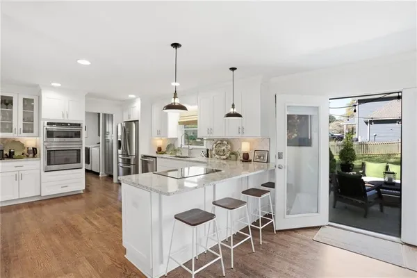 a kitchen with stainless steel appliances kitchen island granite countertop a refrigerator a stove and white cabinets with wooden floor