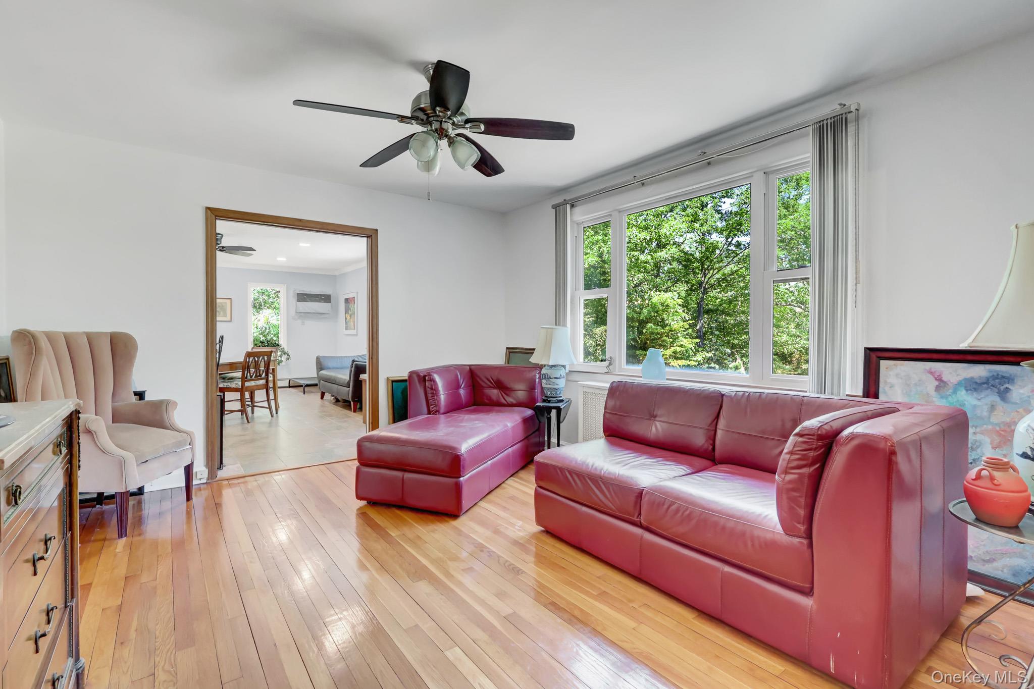 100 Elwood Road Northport, NY 11768 - Photo 12 of 39 Bright living area featuring wood-finish flooring, a ceiling fan, and a large window overlooking natural scenery