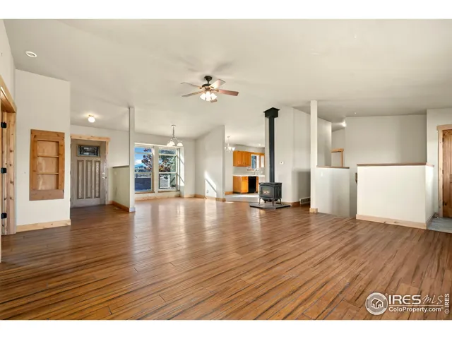 a view of an empty room with wooden floor and a kitchen