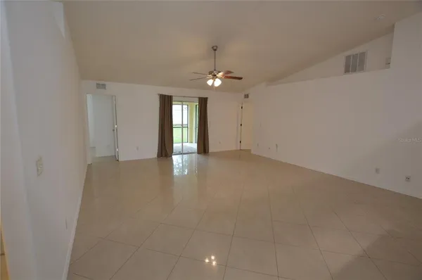 an empty room with chandelier fan and windows