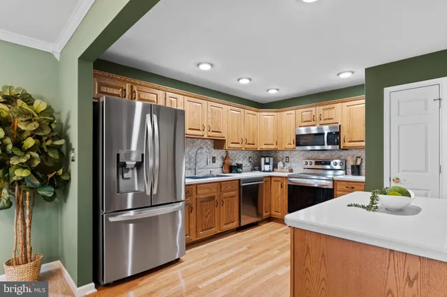 a kitchen with stainless steel appliances granite countertop a refrigerator a sink dishwasher a stove and white countertops with wooden floor