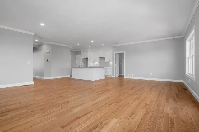 a view of empty room with wooden floor and a kitchen