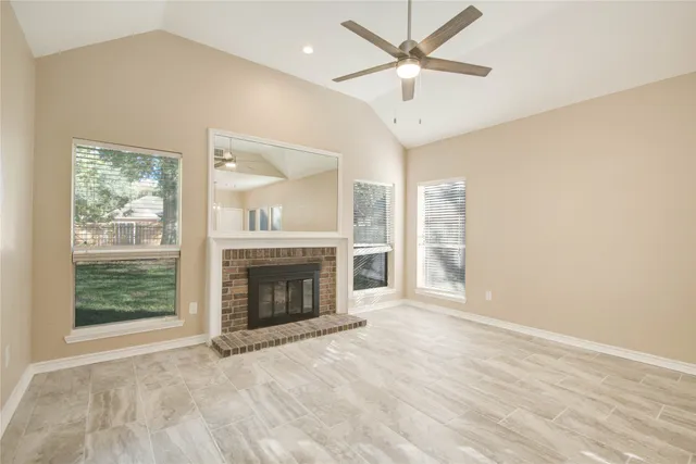 an empty room with windows fireplace and a ceiling fan