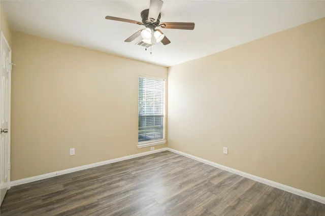 an empty room with wooden floor fan and windows