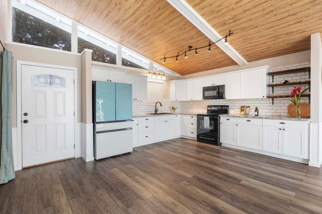 a kitchen with granite countertop a refrigerator oven a sink dishwasher and white cabinets with wooden floor