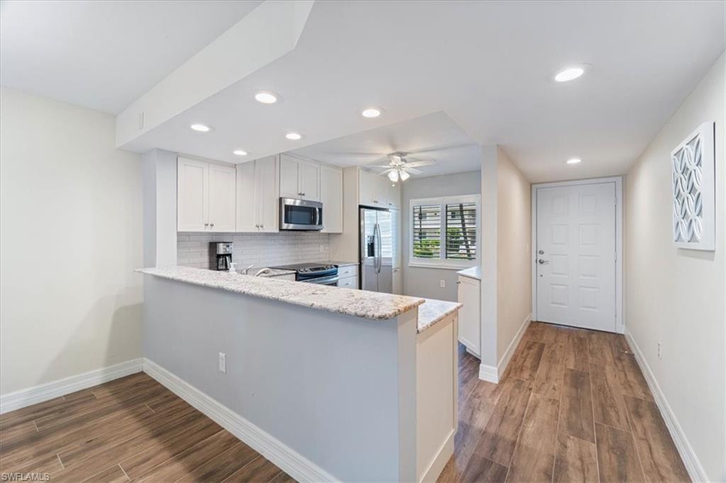 a kitchen with stainless steel appliances granite countertop a refrigerator a sink dishwasher a stove and white countertops with wooden floor