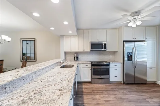 a kitchen with stainless steel appliances granite countertop a refrigerator a sink dishwasher a stove and white countertops with wooden floor