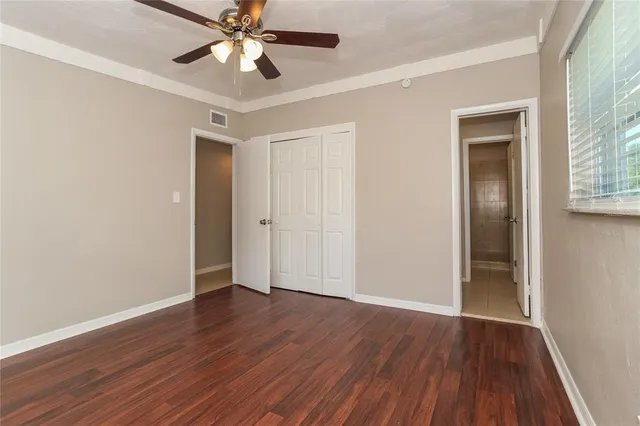 a view of an empty room with wooden floor and a ceiling fan