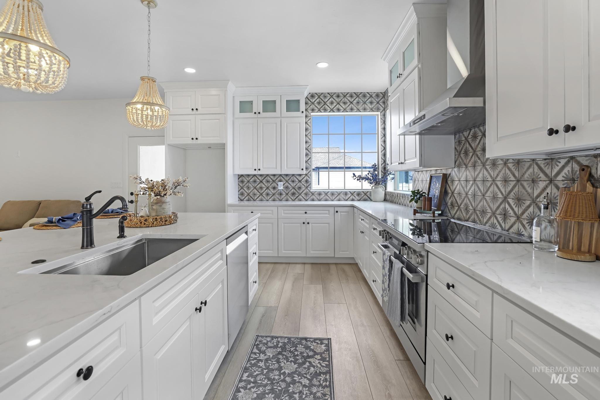 866 Quartz Road Kimberly, ID 83341 - Photo 16 of 48 Kitchen featuring an expansive island with an undermount sink and dark bronze faucet, white cabinetry, a tile backsplash with a geometric pattern, and light wood-finish flooring
