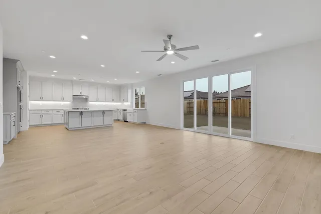 an empty room with wooden floor kitchen view and a window