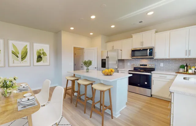 a kitchen with stainless steel appliances a stove a sink a refrigerator a microwave a dining table and chairs with wooden floor