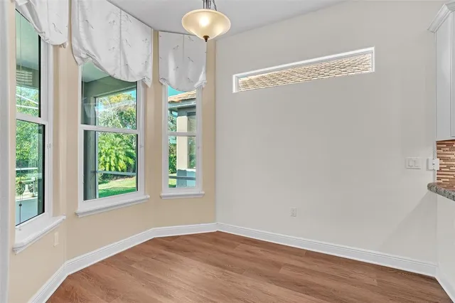 an empty room with wooden floor chandelier fan and windows