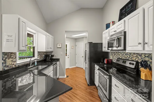 a kitchen with stainless steel appliances a stove a sink a refrigerator white cabinets and wooden floor