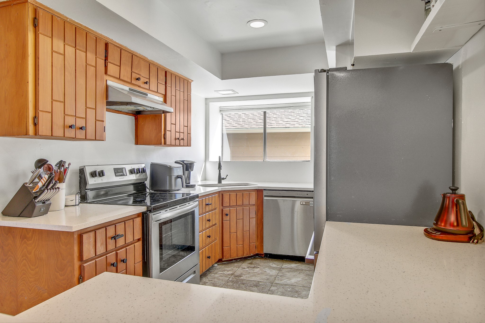 8925 North Plaza, Unit 69 Austin, TX 78753 - Photo 11 of 29 Kitchen featuring stainless steel appliances, brown cabinets, under cabinet range hood, and light stone countertops