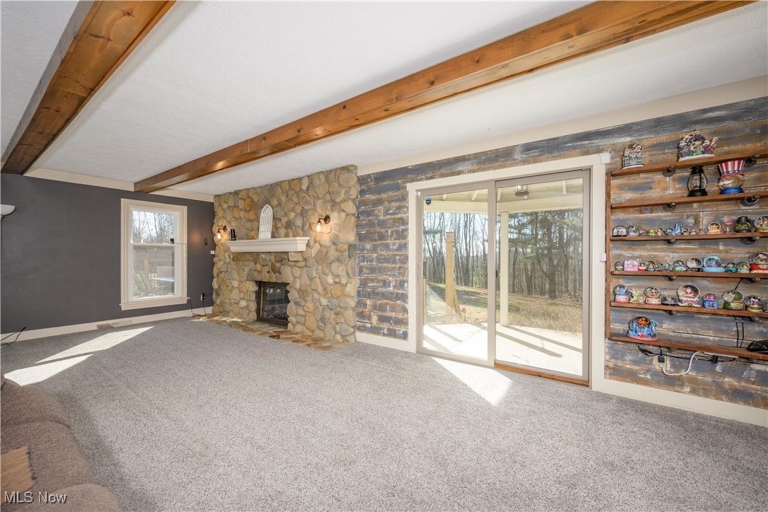 2061 Portage Line Road Mogadore, OH 44260 - Photo 19 of 48 Unfurnished living room with beamed ceiling, a stone fireplace, and carpet flooring
