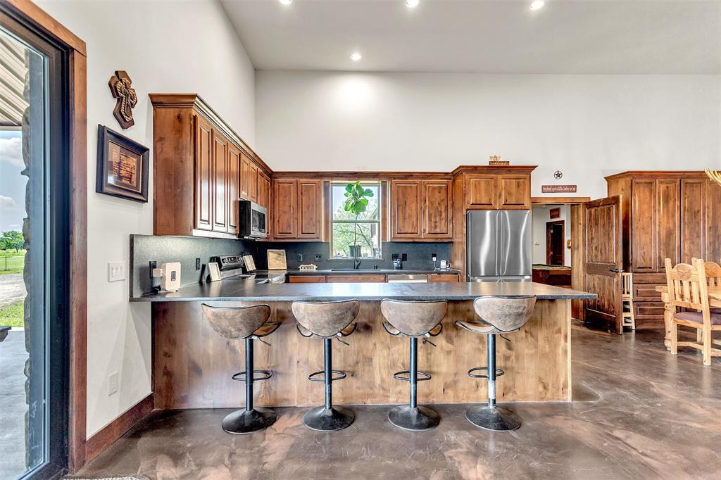13831 Friendship Road Pilot Point, TX 76258 - Photo 30 of 31 Kitchen featuring stainless steel appliances, finished concrete floors, a towering ceiling, leathered granite counter tops and backsplash, bar stools at the peninsula so you can sit and eat or just visit as others cook. dining room and pantry acess is so easy with open floor plan and recessed lighting