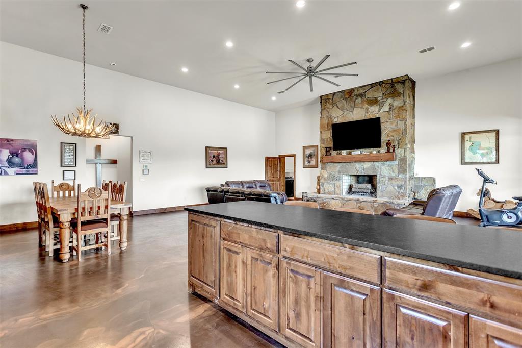 13831 Friendship Road Pilot Point, TX 76258 - Photo 3 of 31 Kitchen with recessed lighting, a ceiling fan, a chandelier, a stone fireplace, and leathered countertops and backsplash, easy access to dining table.