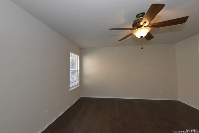 an empty room with wooden floor fan and windows
