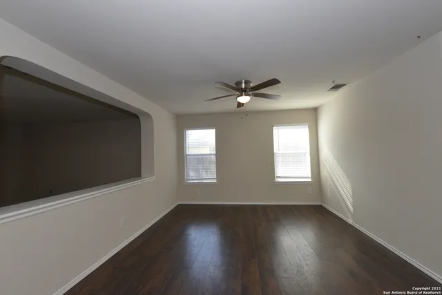an empty room with wooden floor fan and windows