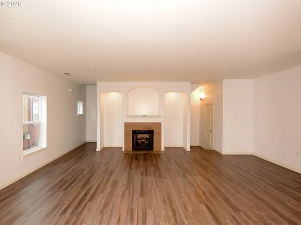 an empty room with wooden floor fireplace and windows